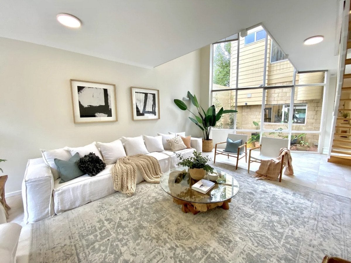 A bright, modern living room featuring a long white sofa with numerous pillows and a textured throw blanket.