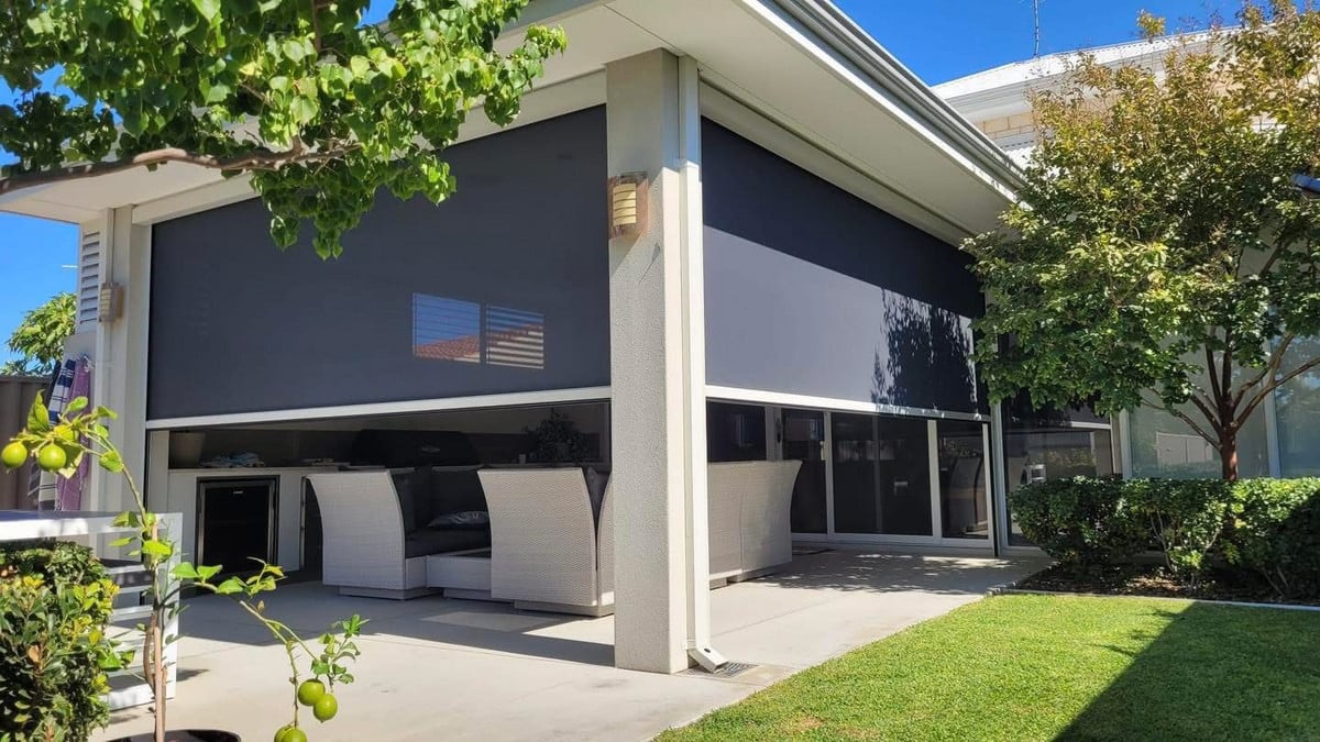 A modern outdoor patio area featuring large charcoal-coloured motorised blinds partially lowered
