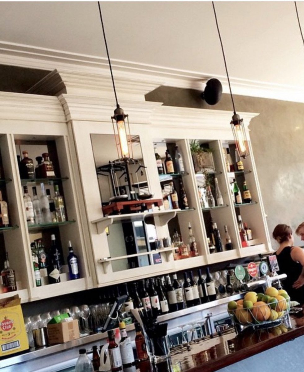 A well-lit bar featuring white shelving stocked with various liquor bottles