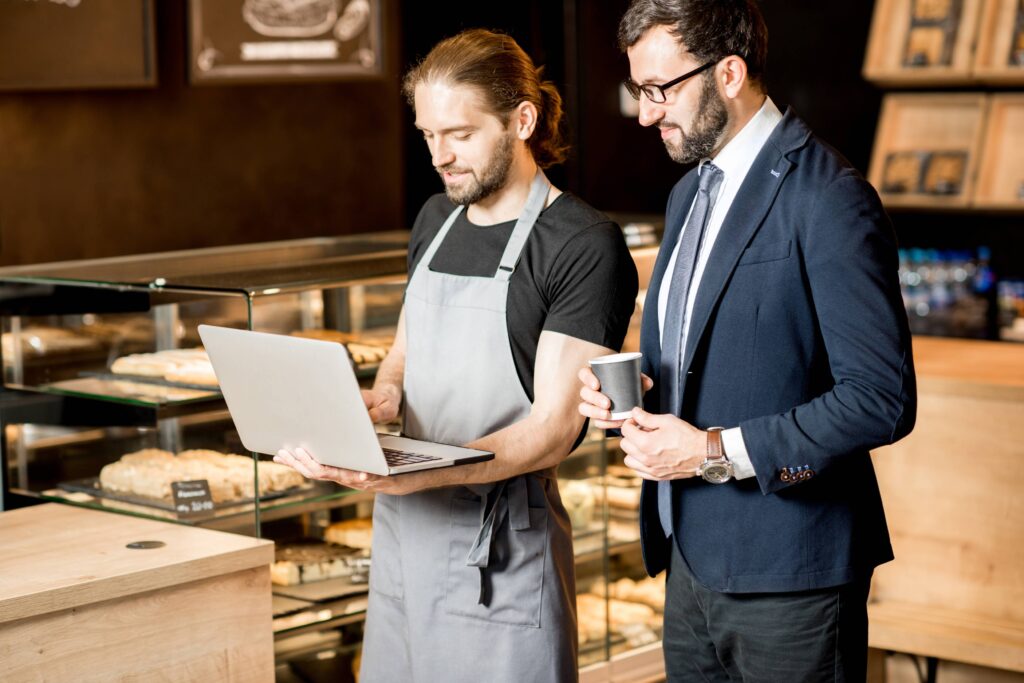 Businessman or store owner and barista working together with laptop